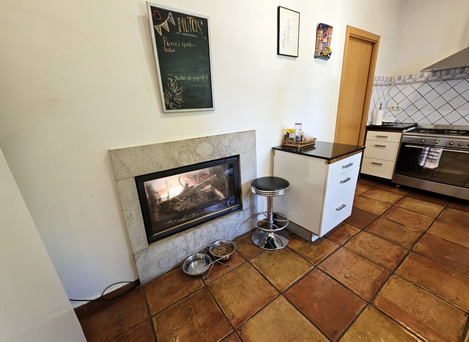 Keuken met handgemaakte terracotta vloertegels en een ingebouwde haard met stenen omlijsting. Voorzien van witte kasten, een donker werkblad en handbeschilderde wandtegels.