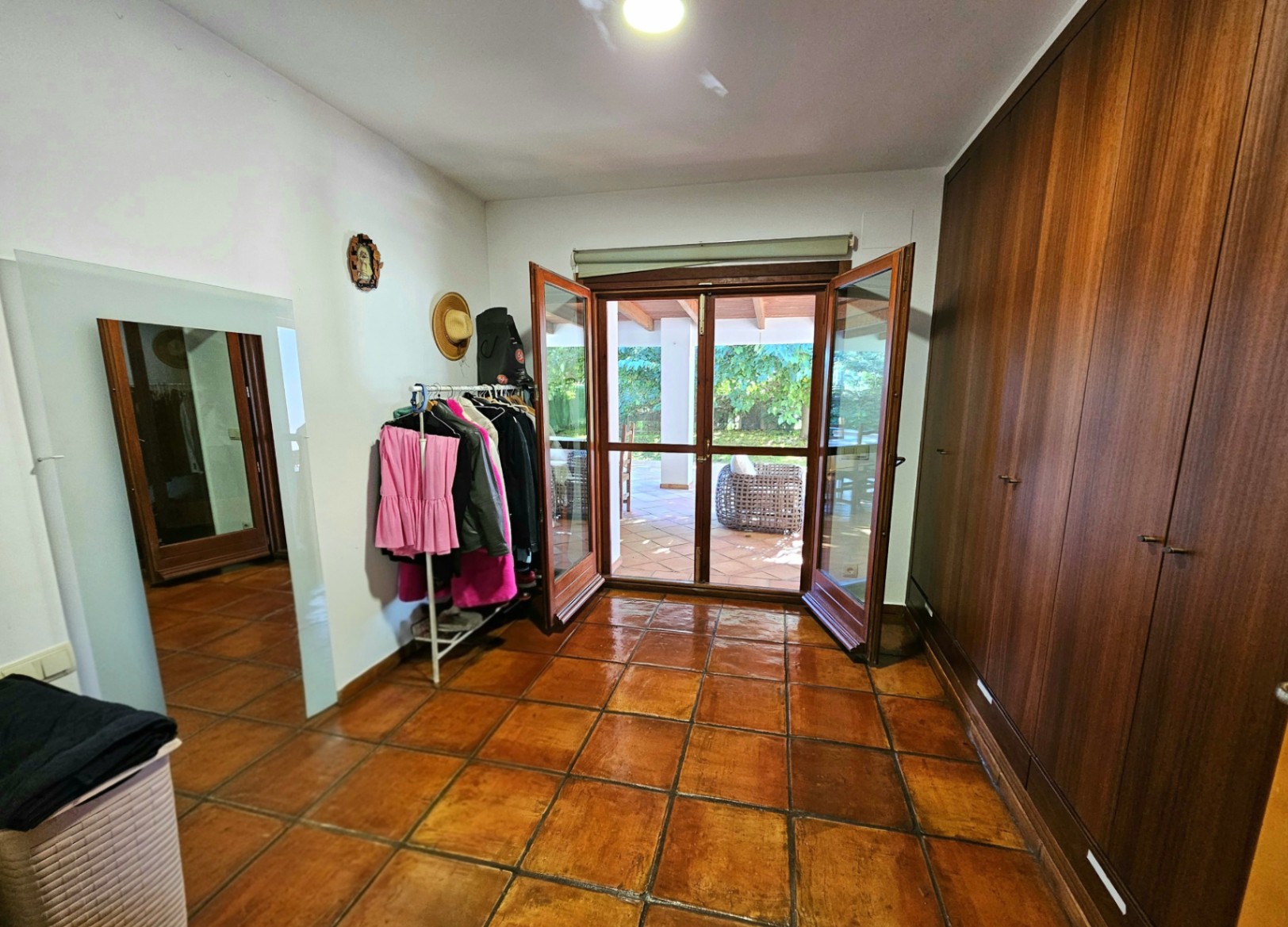 Kleedkamer met grote houten inbouwkasten, handgemaakte terracotta vloertegels en directe toegang tot het overdekte terras via glazen deuren.
