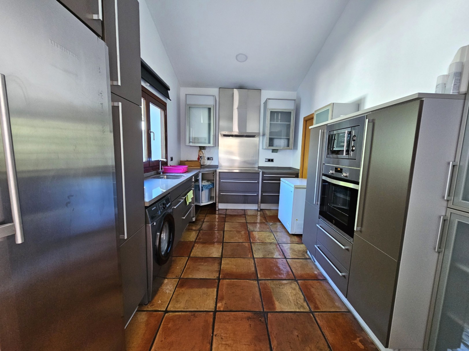 Moderne keuken met matgrijze kasten, roestvrijstalen inbouwapparatuur en handgemaakte terracotta vloertegels die zorgen voor een warme, landelijke uitstraling.