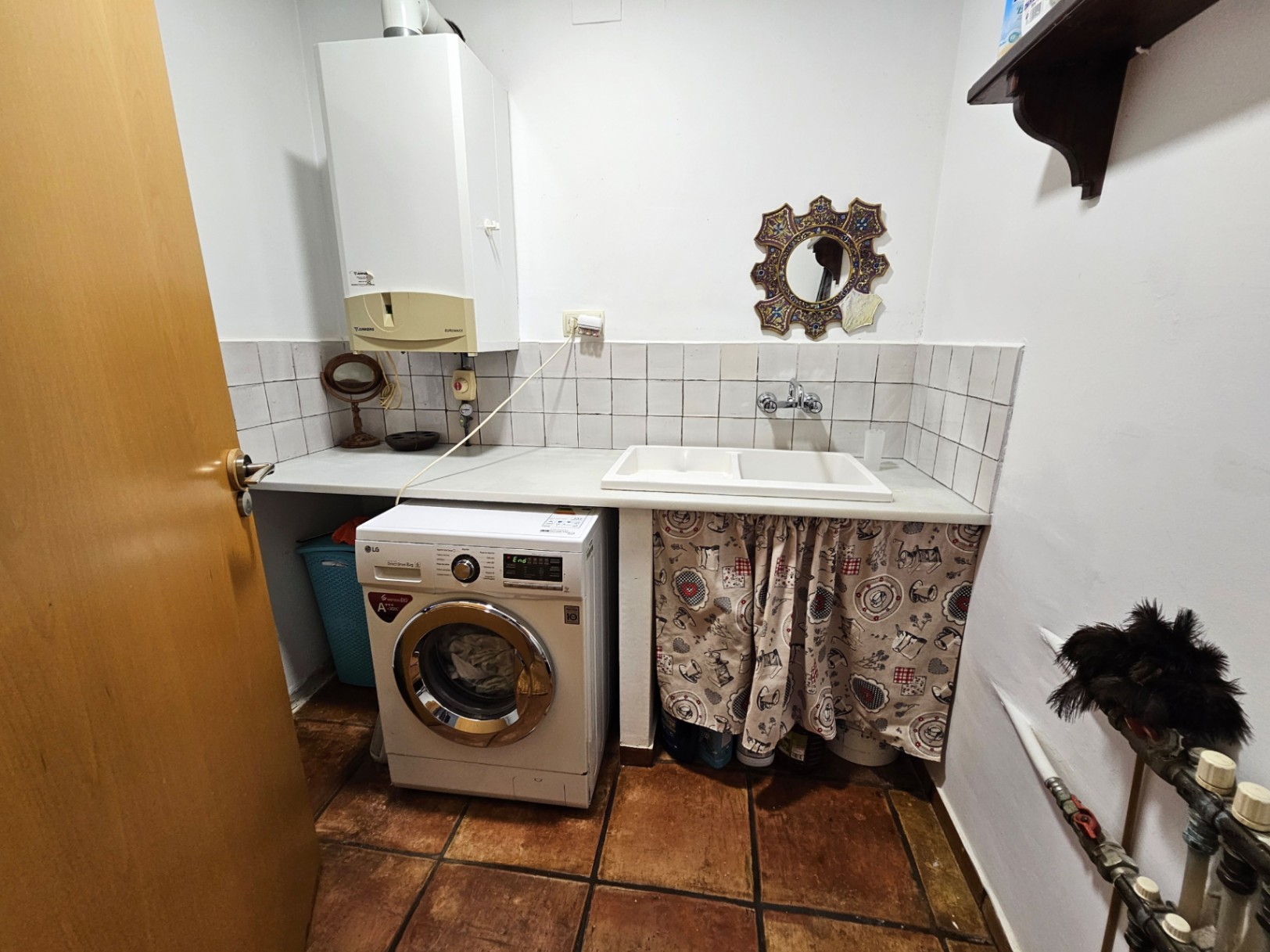 Praktische wasruimte met handgemaakte terracotta vloertegels, voorzien van een wasmachine, dubbele spoelbak en wandgemonteerde cv-ketel.
