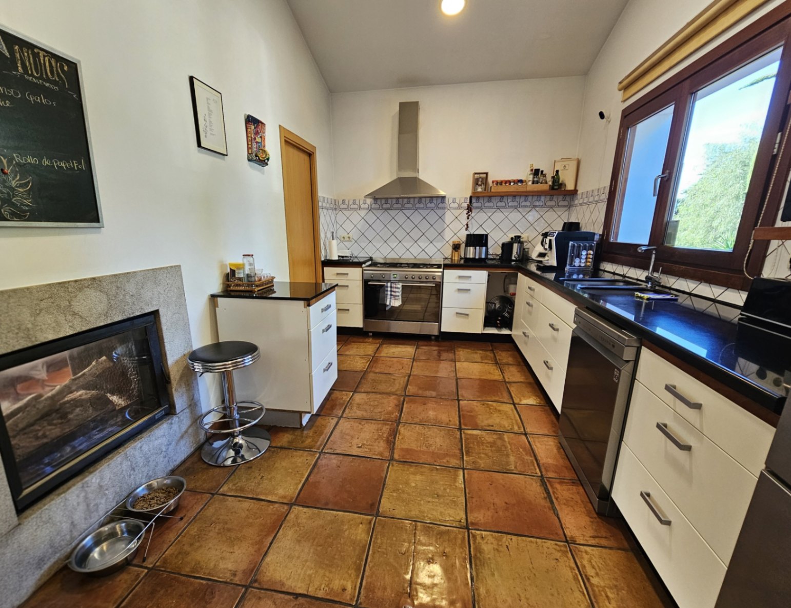 Rustieke keuken met handgemaakte terracotta vloertegels, donkere werkbladen en een tweezijdige open haard geïntegreerd in een natuurstenen muur.