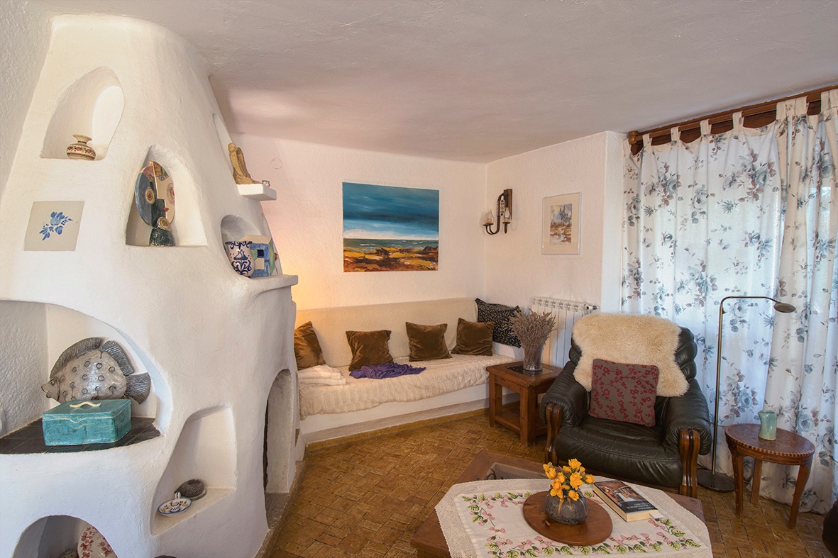 Gezellige woonkamer met een unieke sculpturale witte open haard met nissen, rustieke tegelvloer en een traditionele inrichting.