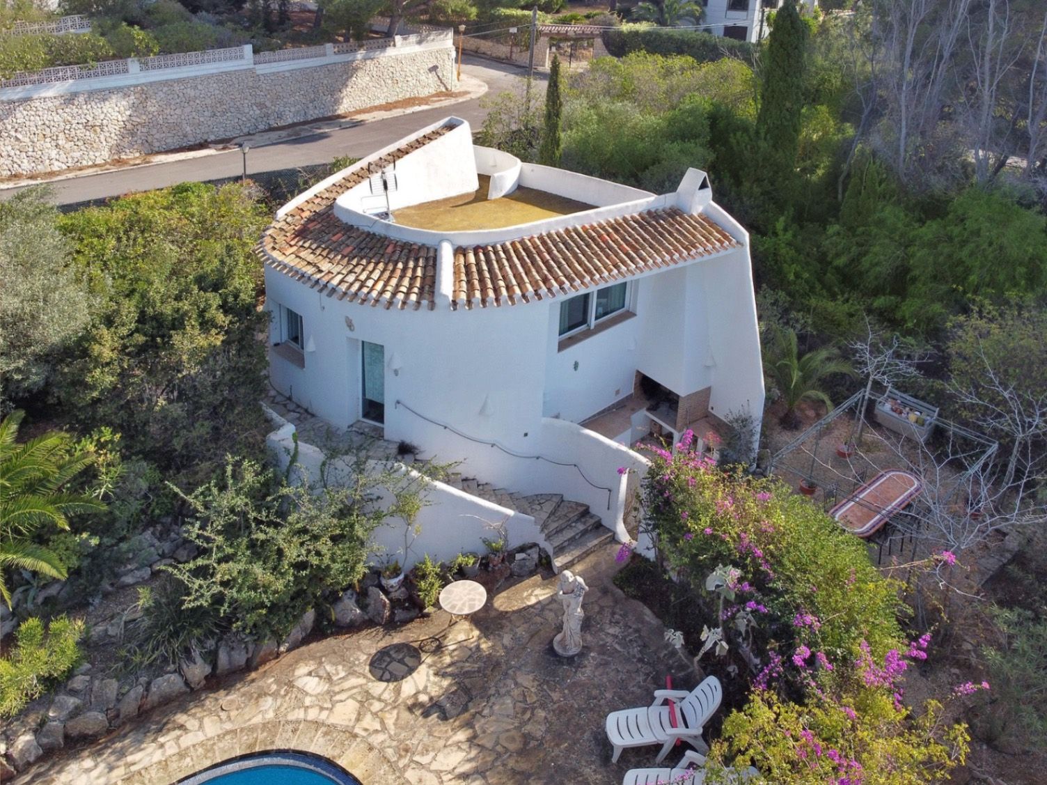 Luchtfoto van de tweede villa met gebogen witte muren, een ingebouwde barbecueplaats, stenen trappen en een geplaveid terras omgeven door mediterrane tuinen.
