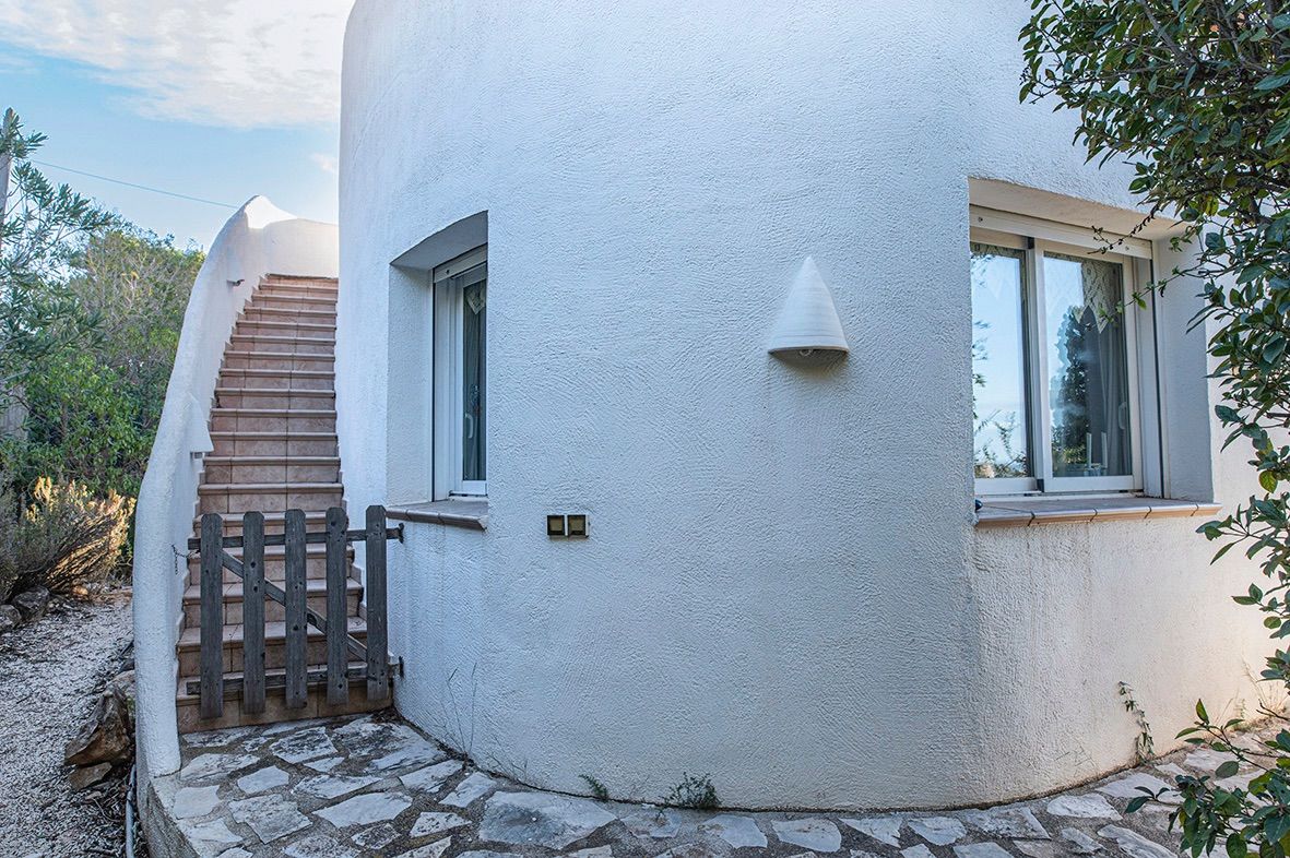 Mediterrane gebogen gevel met een betegelde buitentrap, een rustiek houten hekje en ramen met dubbele beglazing op een natuurstenen vloer.