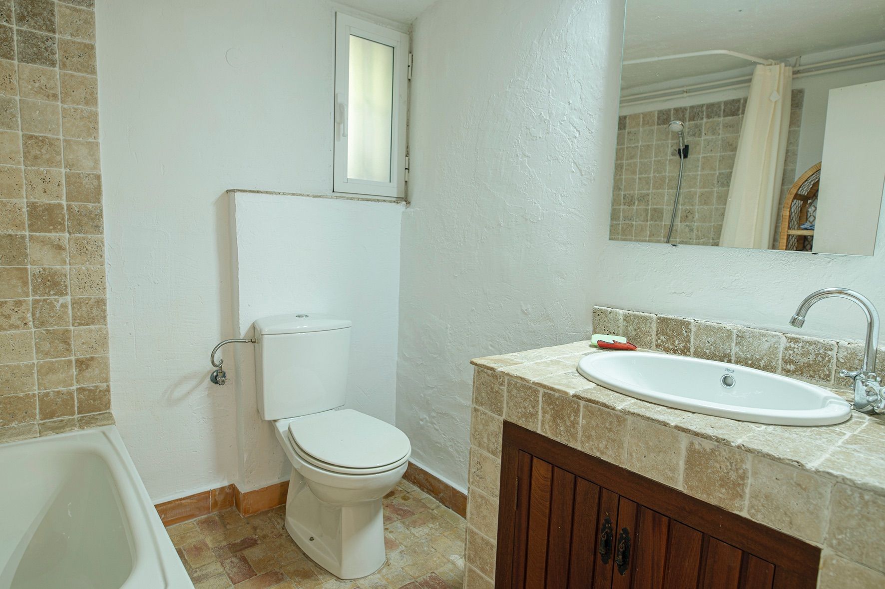 Rustieke badkamer met een natuurstenen wastafelblad, donkerhouten kastje, wit sanitair en een ingebouwd ligbad.