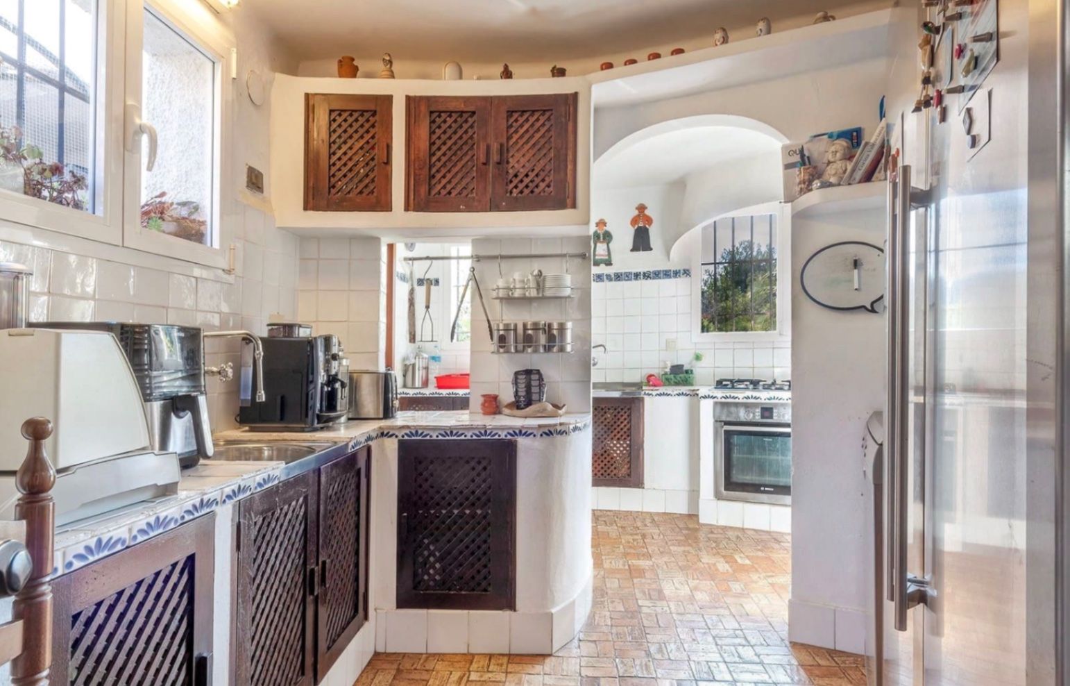Rustieke keuken met donkerhouten vlechtwerk kasten, wit-blauw betegelde werkbladen en een traditionele terracotta vloer met veel natuurlijk licht.