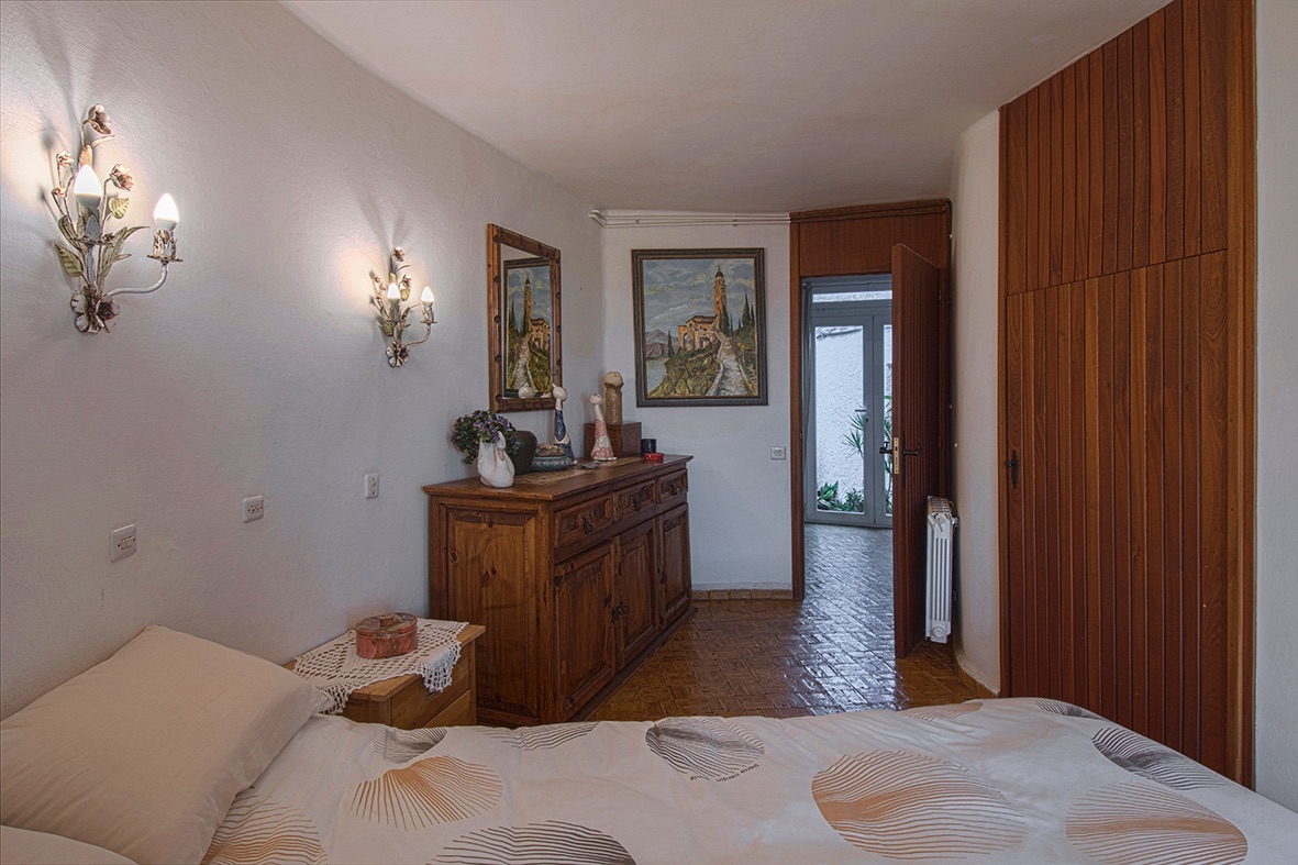 Rustieke slaapkamer met een tegelvloer, ingebouwde houten kledingkast en decoratieve wandlampen. De kamer is voorzien van een massief houten dressoir en directe toegang naar buiten.