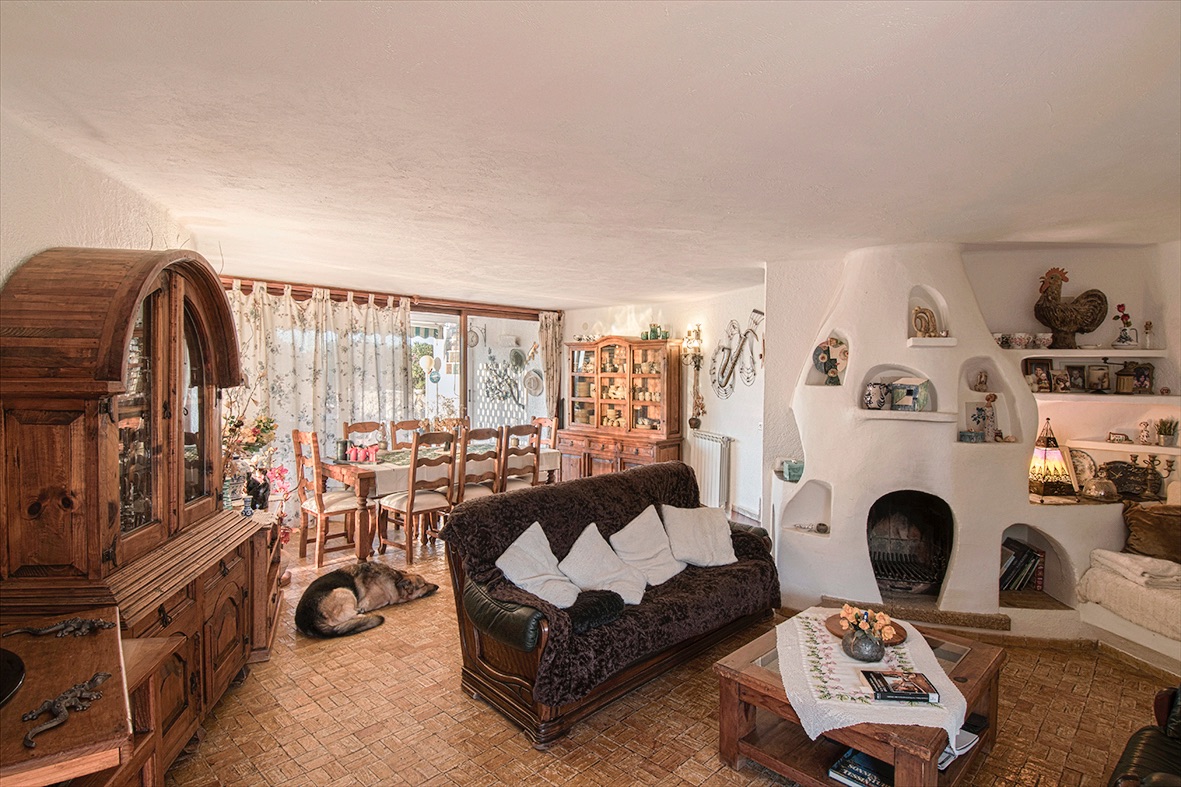 Rustieke woon- en eetkamer met een unieke witte sculpturale open haard, massief houten meubilair en een traditionele terracotta tegelvloer.