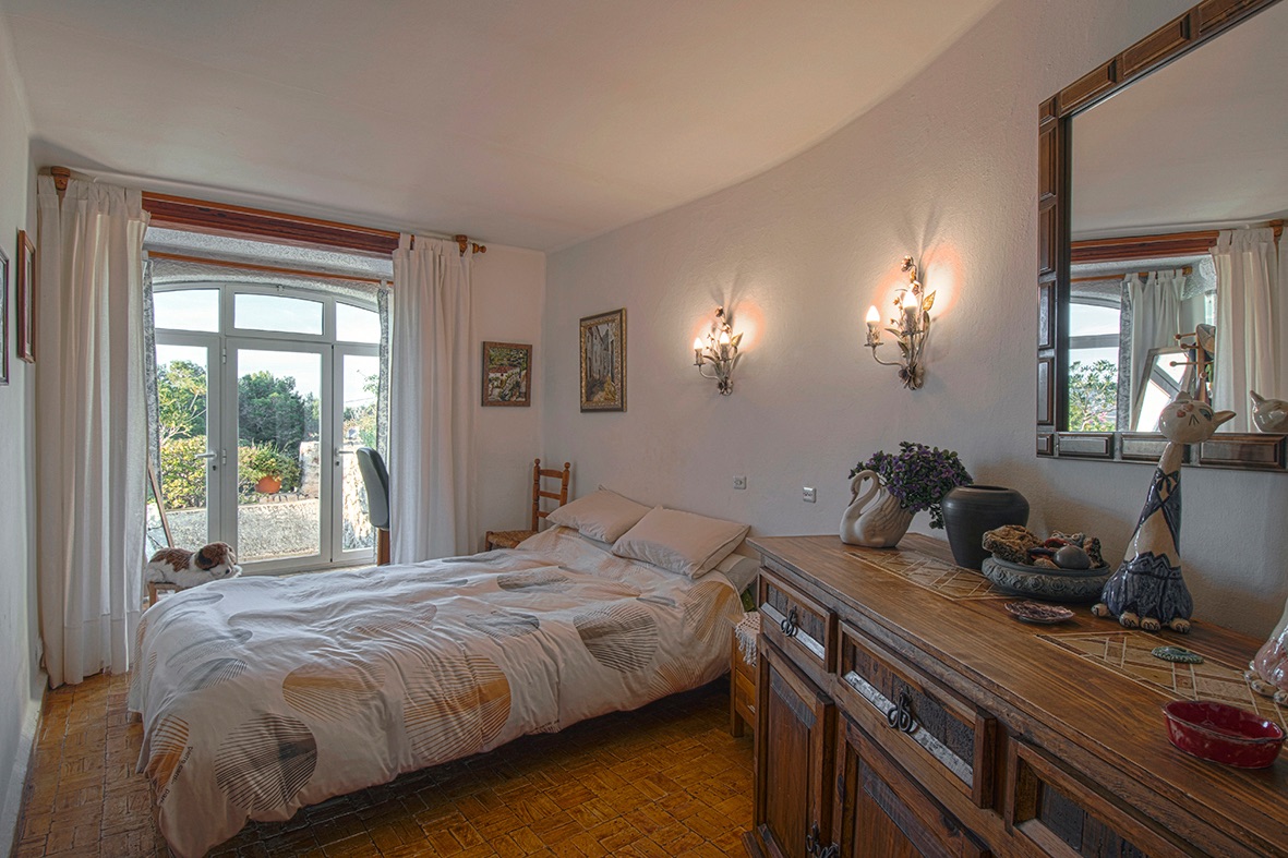 Traditionele slaapkamer met terracotta tegelvloer, rustieke houten meubels en een boogvormige glazen deur die directe toegang tot de tuin biedt.