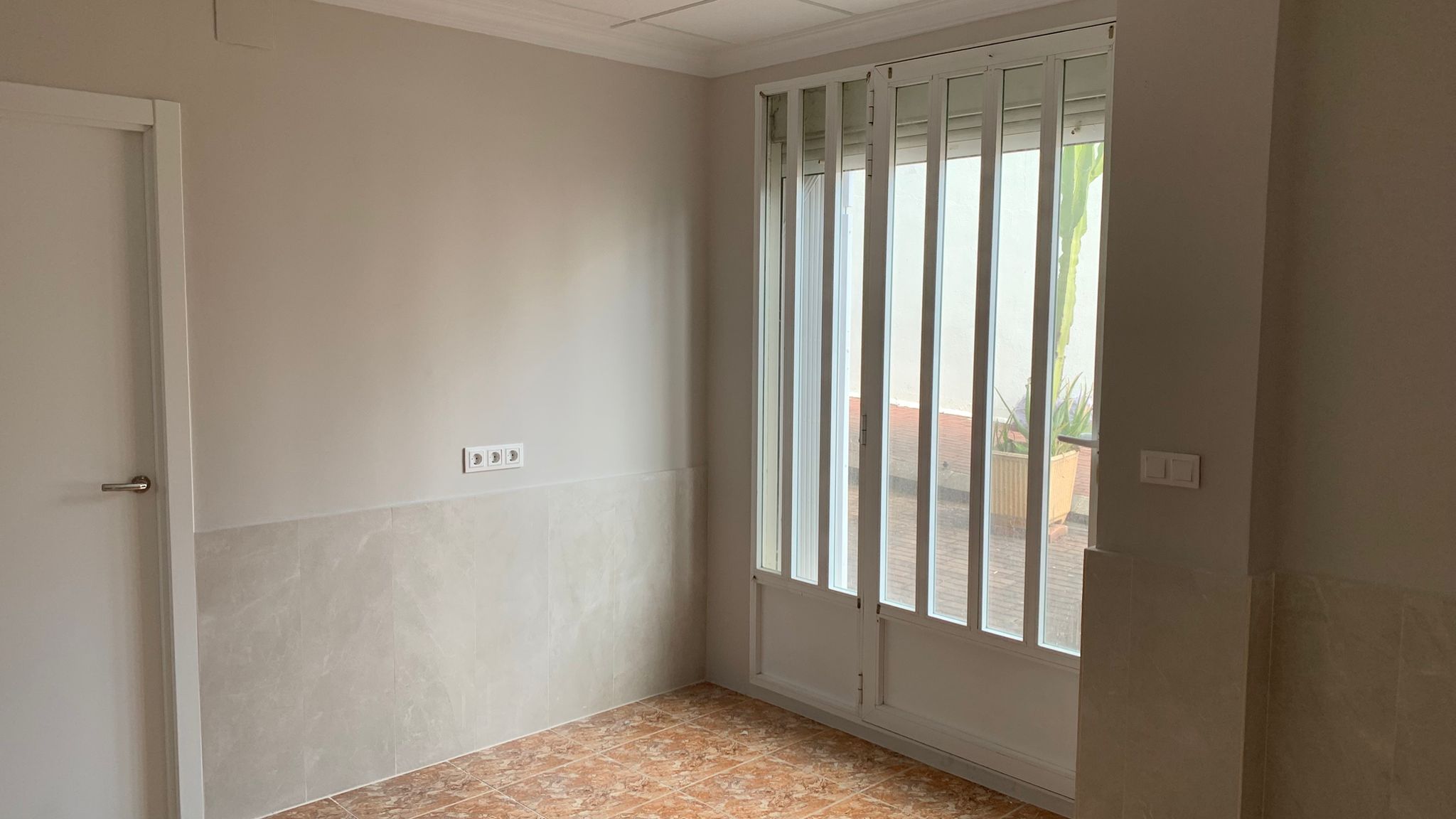 Binnenruimte met terracotta vloertegels, wandtegels met marmerlook en een glazen deur met veiligheidshekwerk die toegang geeft tot de patio.