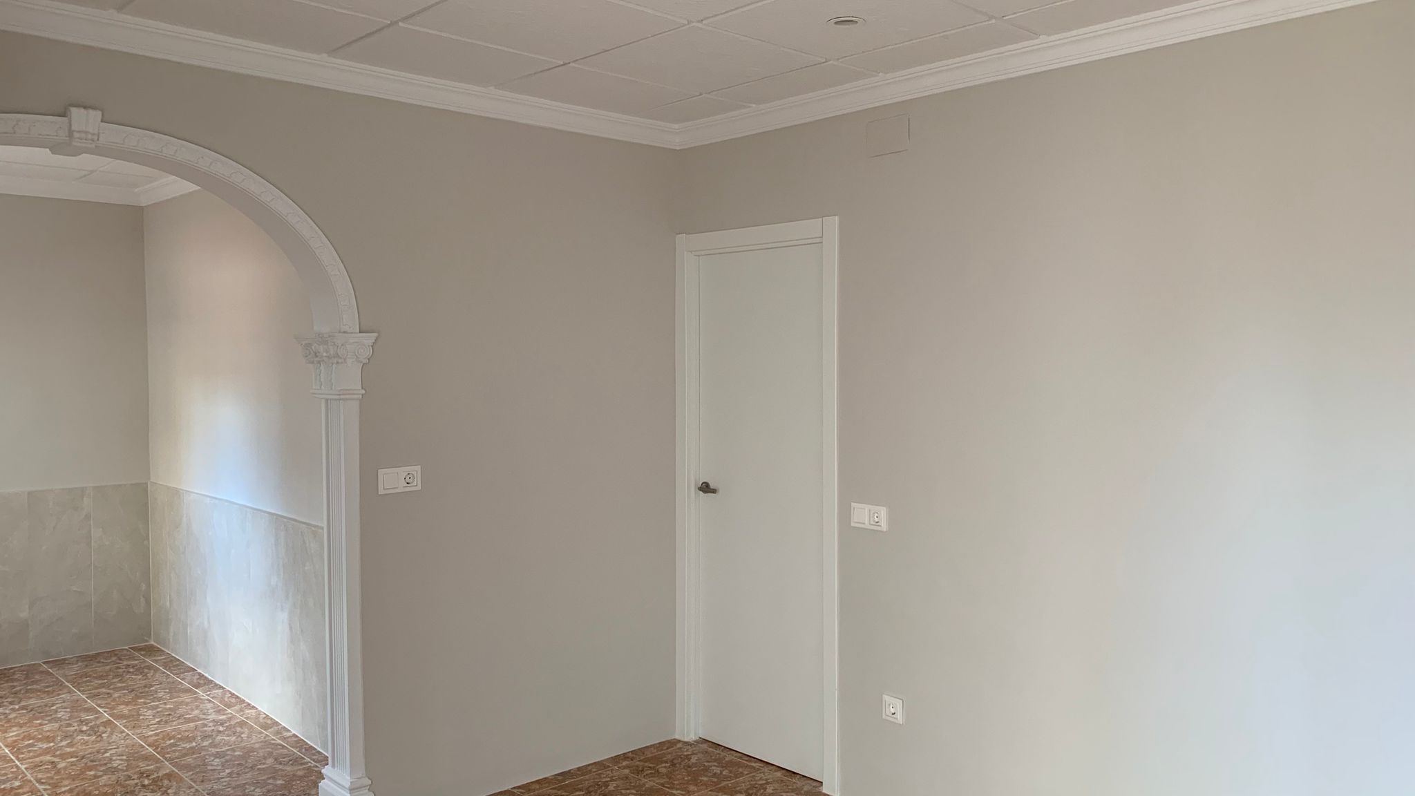Gerenoveerd interieur met een decoratieve klassieke boog, muren in neutrale tinten, keramische tegelvloer en een systeemplafond met elegante sierlijsten.