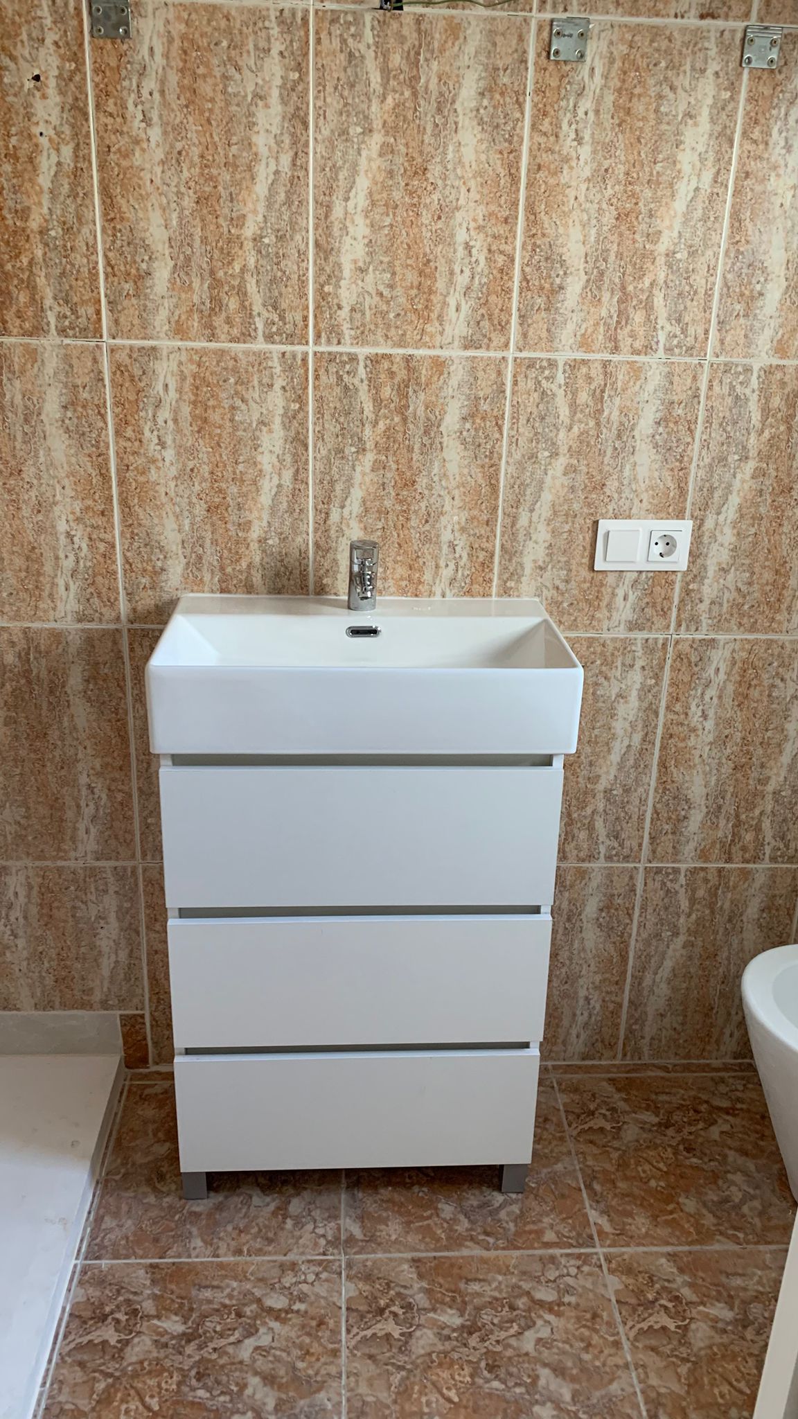 Modern wit badkamermeubel met drie lades en geïntegreerde wastafel, afgewerkt met aardetinten tegels met marmerlook op wand en vloer.