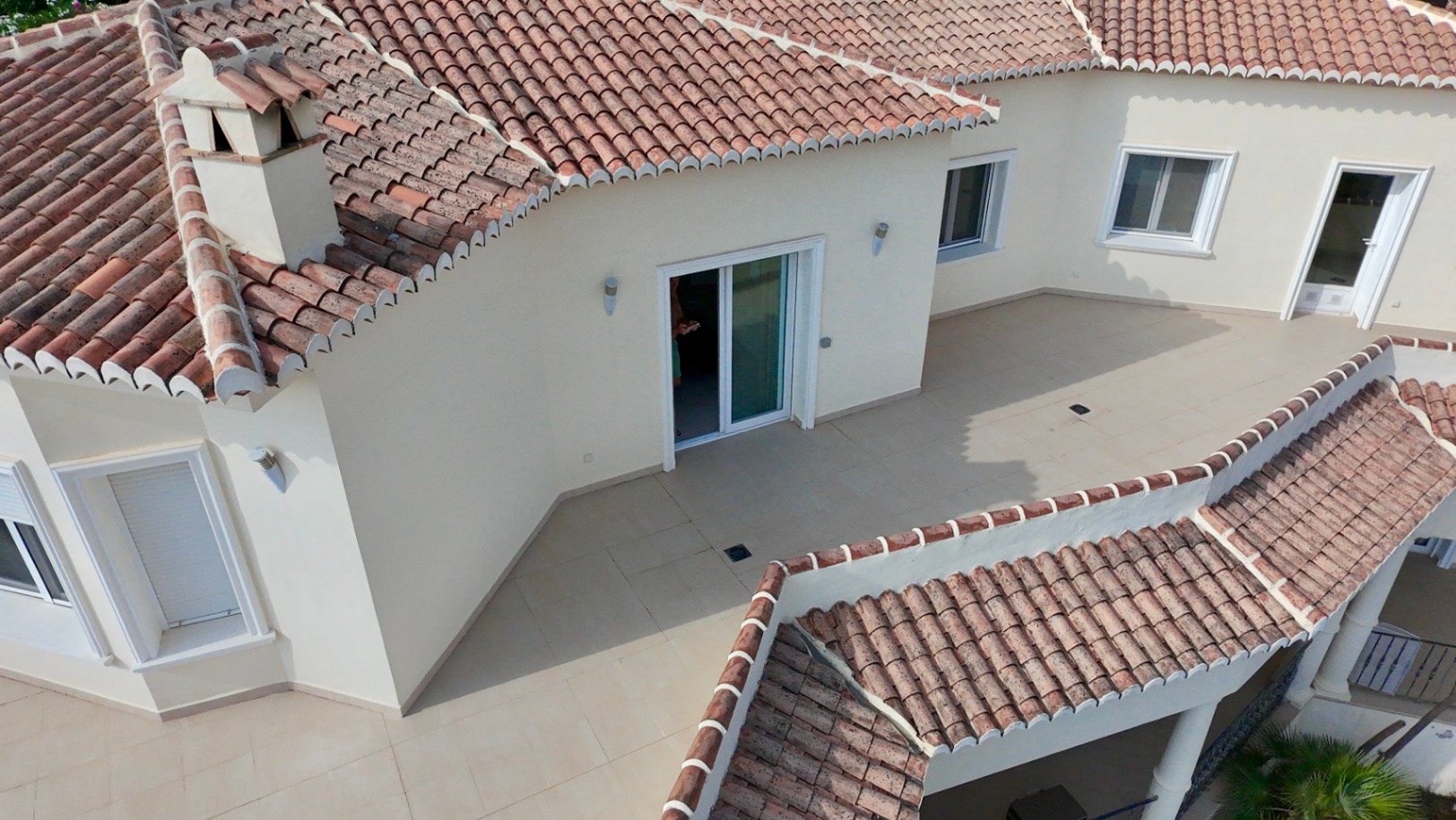 Bovenaanzicht van het boventerras en het dak met terracotta pannen, voorzien van wit raamwerk en een neutrale tegelvloer in een gelaagde architectuur.