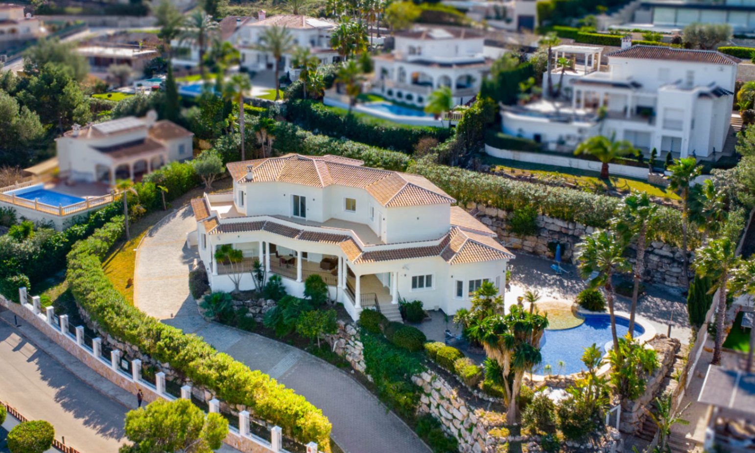 Luchtfoto van de villa in Piver, Jávea, met de mediterrane architectuur, pannendaken en het niervormige zwembad omgeven door een volgroeide tuin.