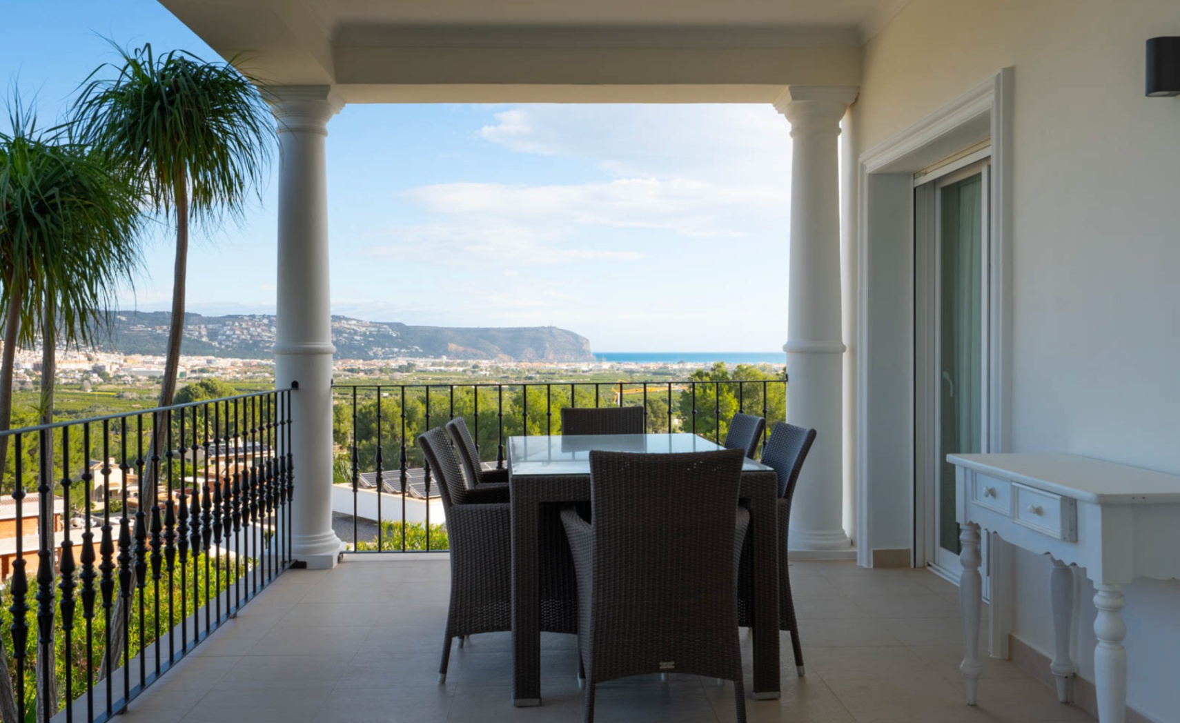 Overdekt terras met klassieke zuilen, smeedijzeren balustrade en een eethoek met panoramisch uitzicht over de vallei van Jávea en de Middellandse Zee.