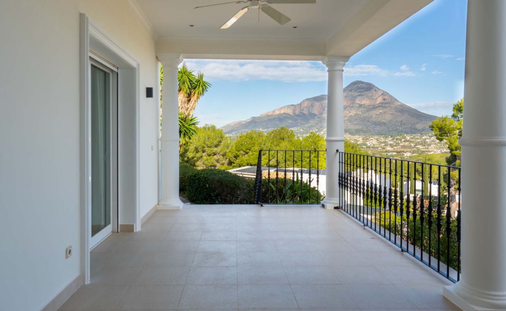 Overdekt terras met witte kolommen en smeedijzeren balustrade, met een weids uitzicht op de Montgó-berg en de groene vallei van Jávea.