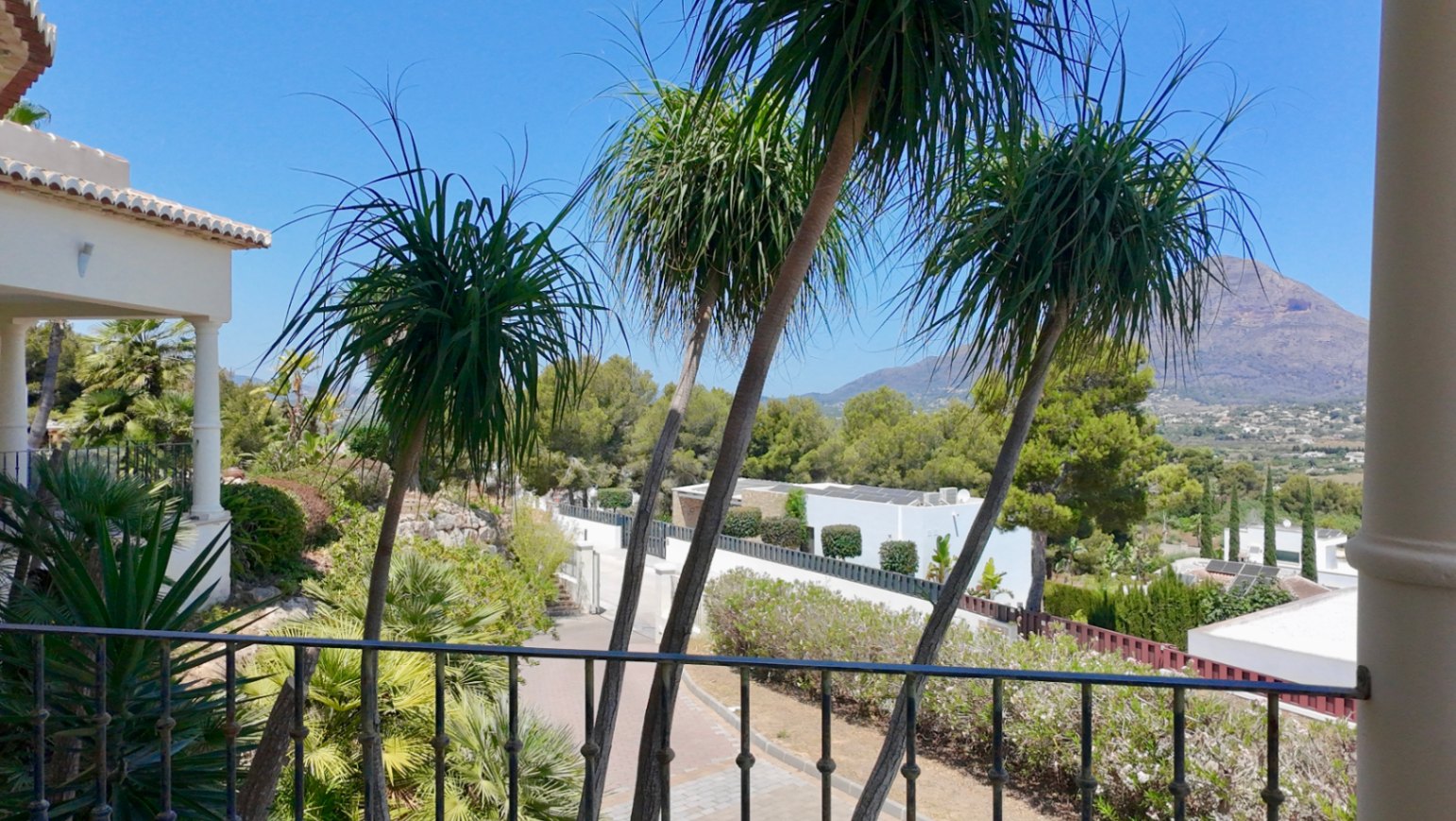 Uitzicht vanaf het bovenste terras met smeedijzeren balustrade, sierlijke palmbomen en een panoramisch zicht op de Montgó-berg en de vallei.